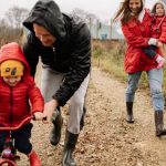 Family enjoying a joyful autumn walk along a rustic dirt road in vibrant outfits.